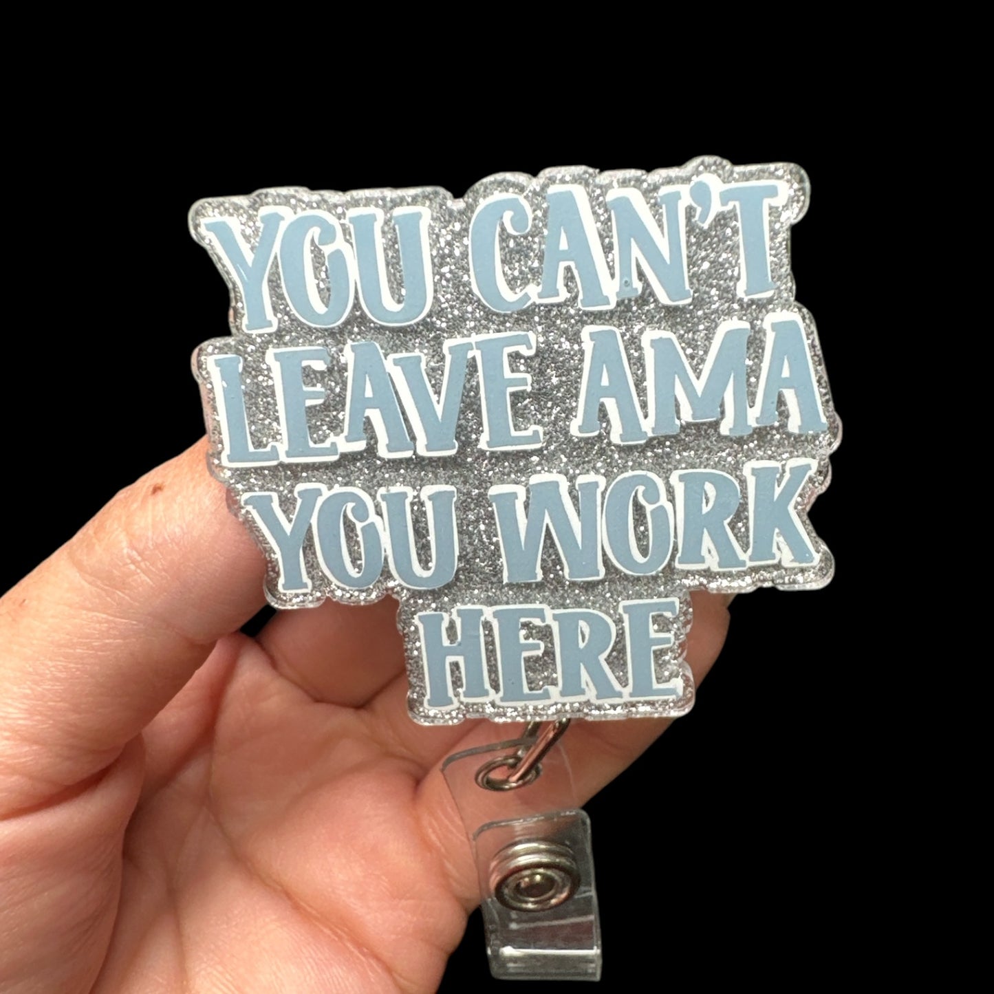 A badge reel with the text 'YOU CAN'T LEAVE AMA YOU WORK HERE' printed on it.