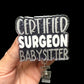 A hand holding a badge reel with the text 'CERTIFIED SURGEON BABYSITTER' on it.