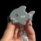 A gray shark-shaped badge reel with a clip attached.
