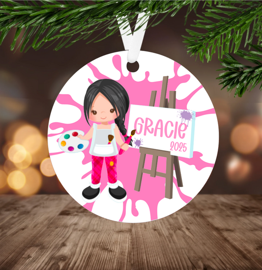 Decorative Christmas ornament with a  girl painting, hanging on a tree branch.