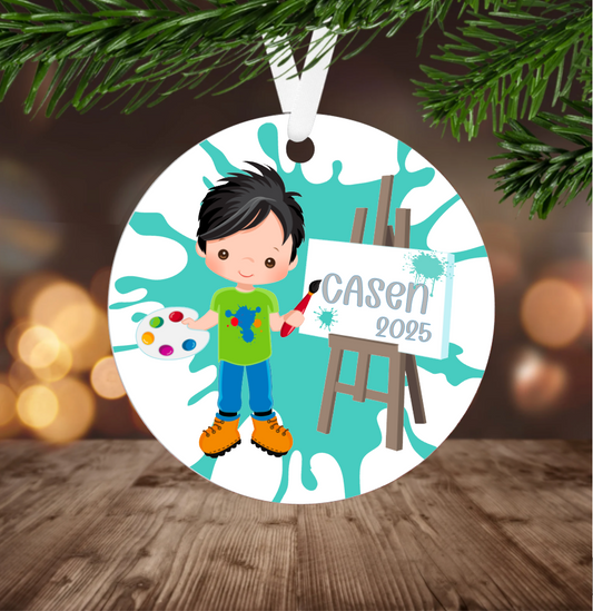 Little boy Christmas ornament with a child holding art supplies and an easel, hanging on a Christmas tree.