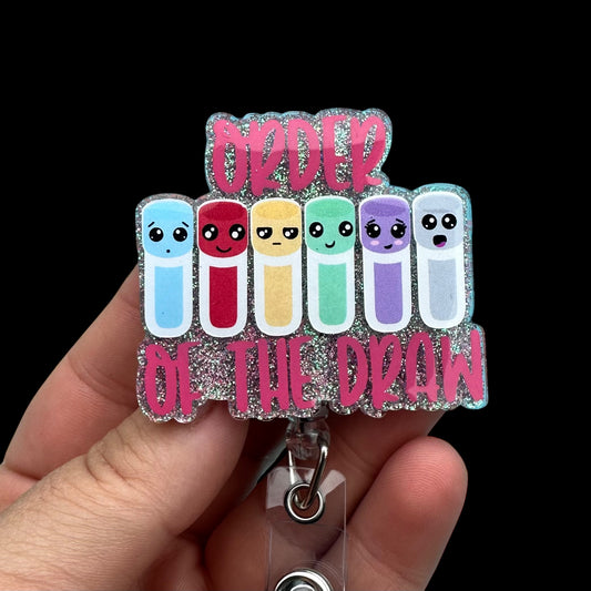 Colorful badge holder with cartoon faces and text "order of the draw"