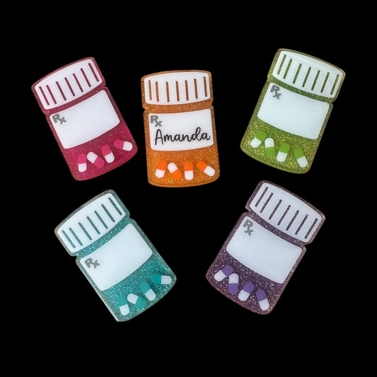 A collection of colorful pill bottle-shaped badge reels with glittery surfaces, each labeled with different names.