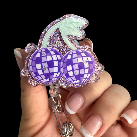 A retractable badge reel with a purple cherry design, decorated with purple and clear crystals.