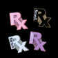 A collection of personalized badge reels with glittery pink 'RX' symbol, customized with names and in various colors including pink, black, silver, and purple.
