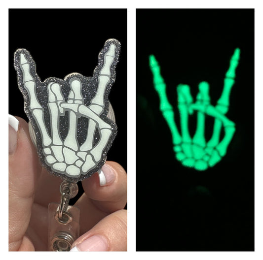 A badge reel with a skeleton hand design that glows in the dark, held in a person's hand.