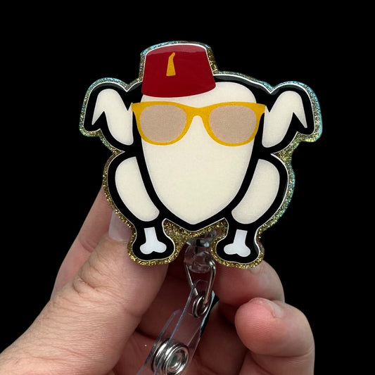 Decorative badge with cartoon character (turkey) wearing a red hat and yellow sunglasses held by a hand against a black background.