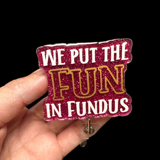 A pink badge reel with the text 'WE PUT THE FUN IN FUNDUS' in glittery gold and white letters.