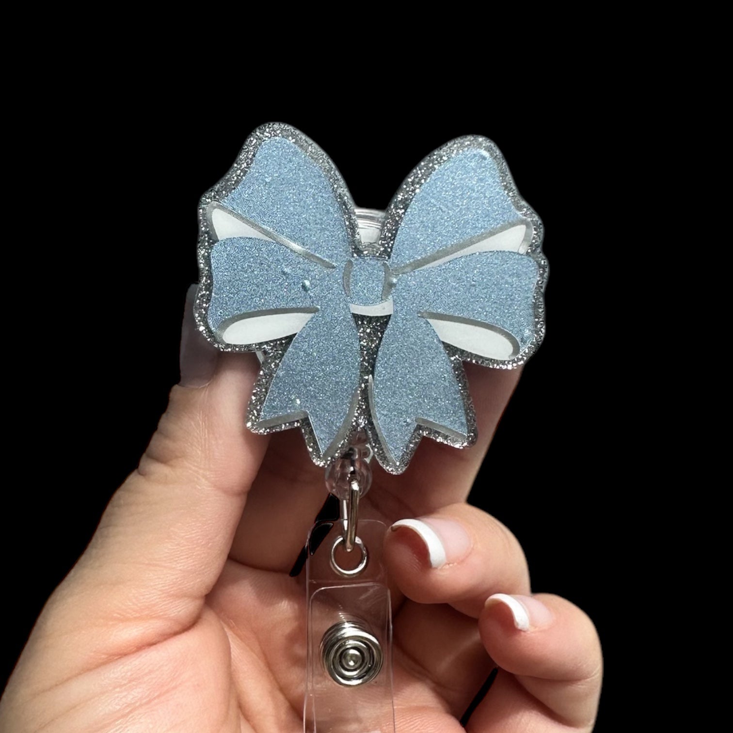 A blue bow-shaped badge reel holder being held in a hand, with a retractable clip.