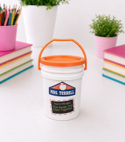 White bucket with orange lid labeled on a white surface with books and plants in the background.